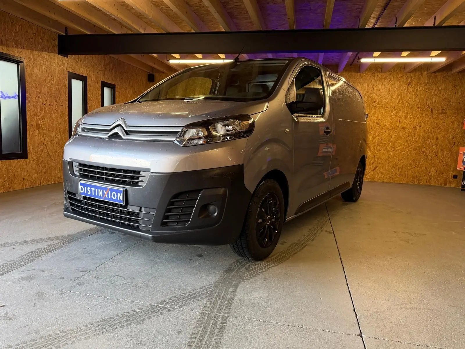 Vue 3/4 avant droit d'un Citroën Jumpy gris métallisé 2022 dans un garage en bois, avec calandre noire et jantes foncées.