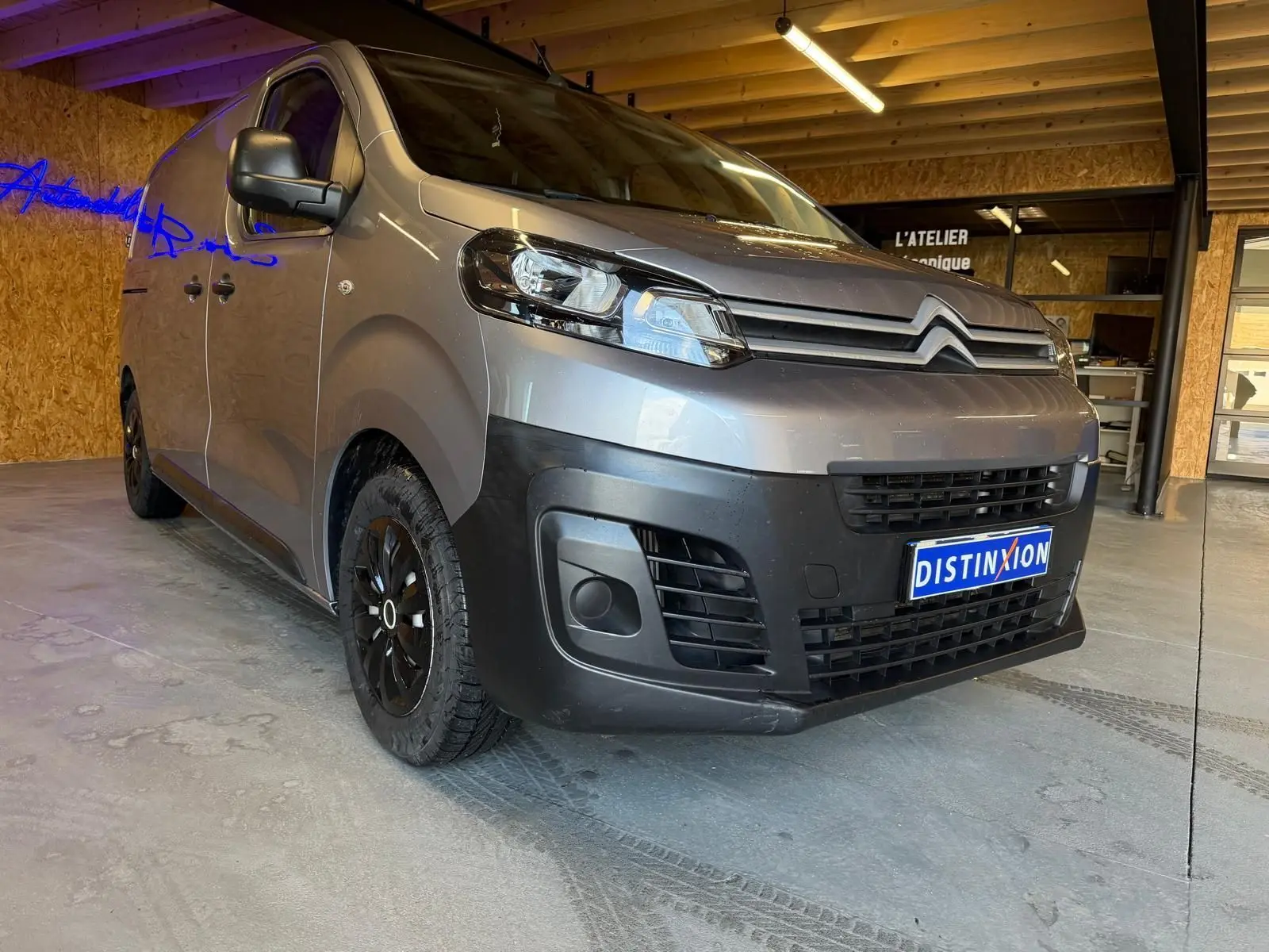 Vue 3/4 avant gauche d'un Citroën Jumpy gris métallisé 2022 avec calandre noire et jantes noires en intérieur d'atelier.