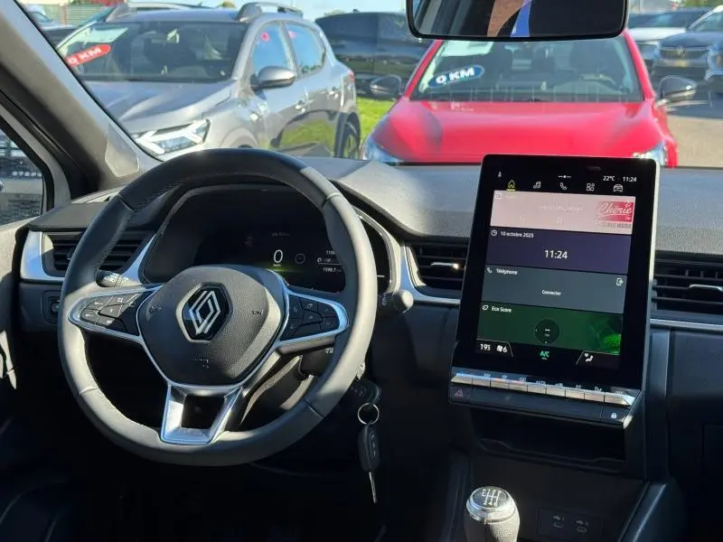 Vue intérieure centrée sur le volant Renault et l’écran tactile vertical du Captur blanc nacré, avec levier de vitesse manuel visible.