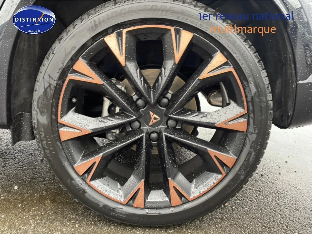 Gros plan sur la jante noire et cuivre du CUPRA Formentor gris Graphene, avec pneus Bridgestone mouillés.