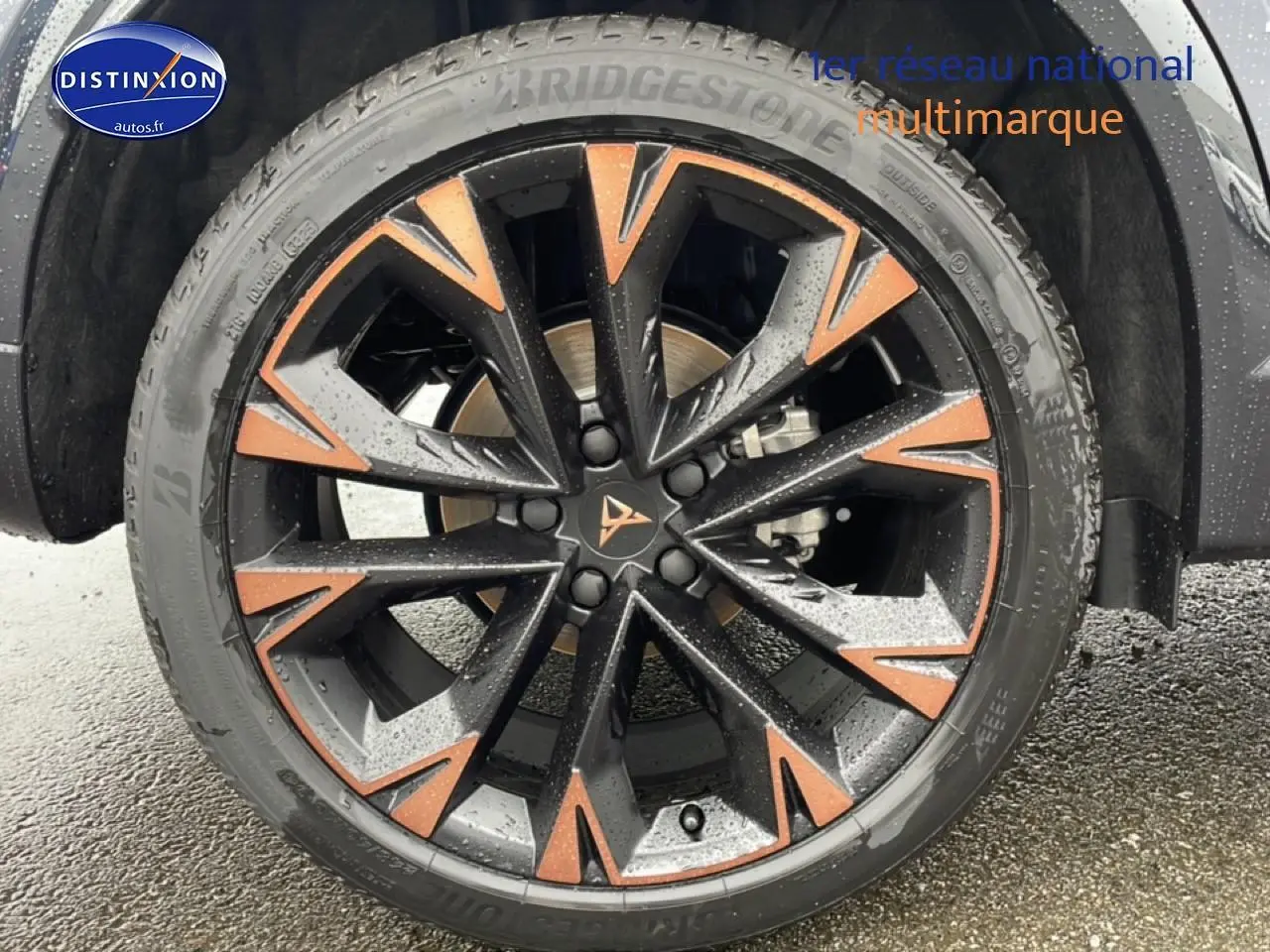 Gros plan sur la jante noire et cuivre du CUPRA Formentor 2.0 TDI 150 DSG7 gris graphene, avec pneu Bridgestone humide.
