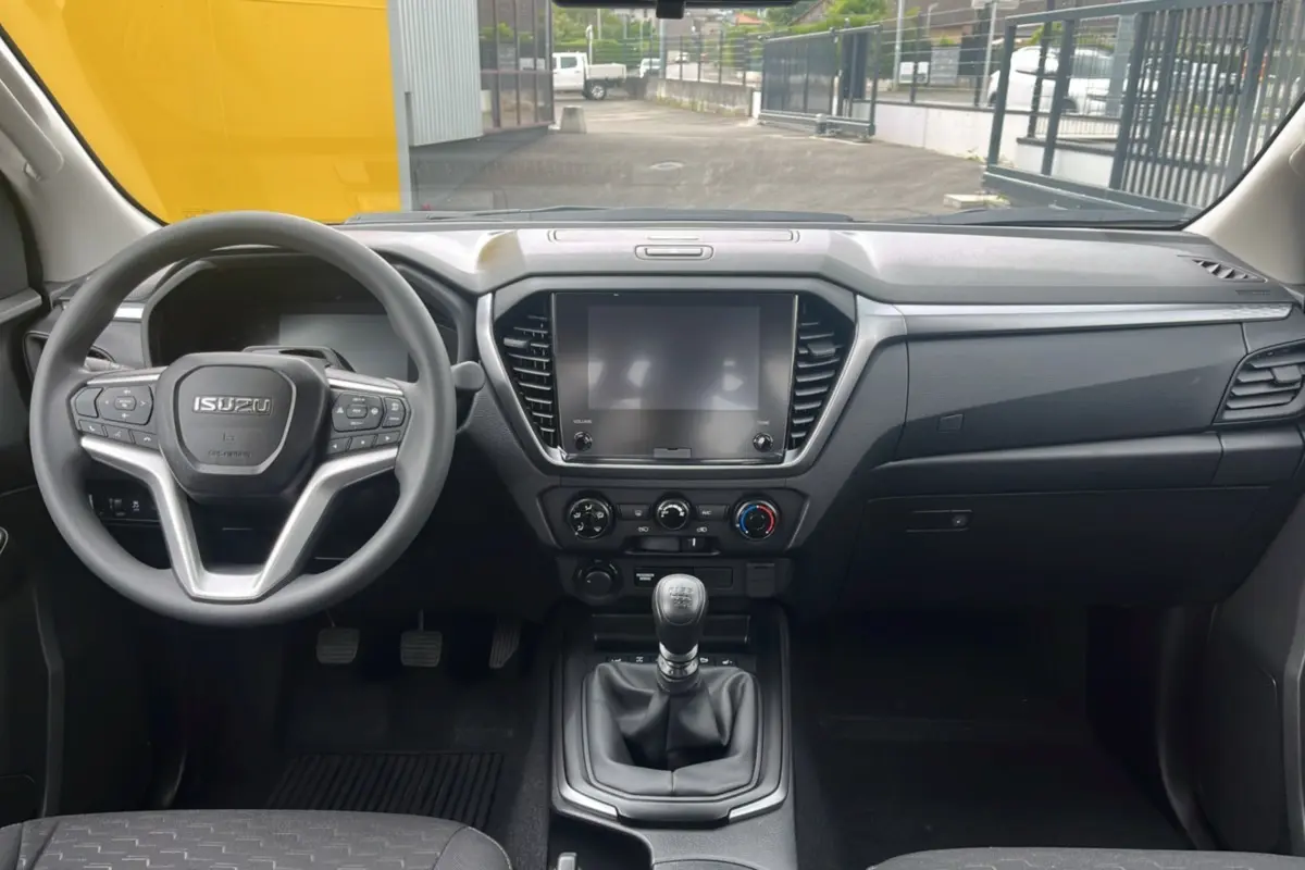 Vue intérieure avant de l'Isuzu D-MAX 2026 avec tableau de bord noir, volant multifonctions et boîte manuelle six vitesses.