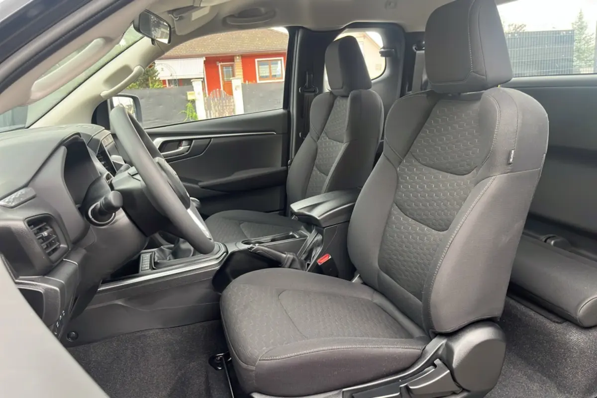 Vue intérieure côté conducteur de l'Isuzu D-MAX 2026 avec sièges tissu gris et accoudoir central avant.