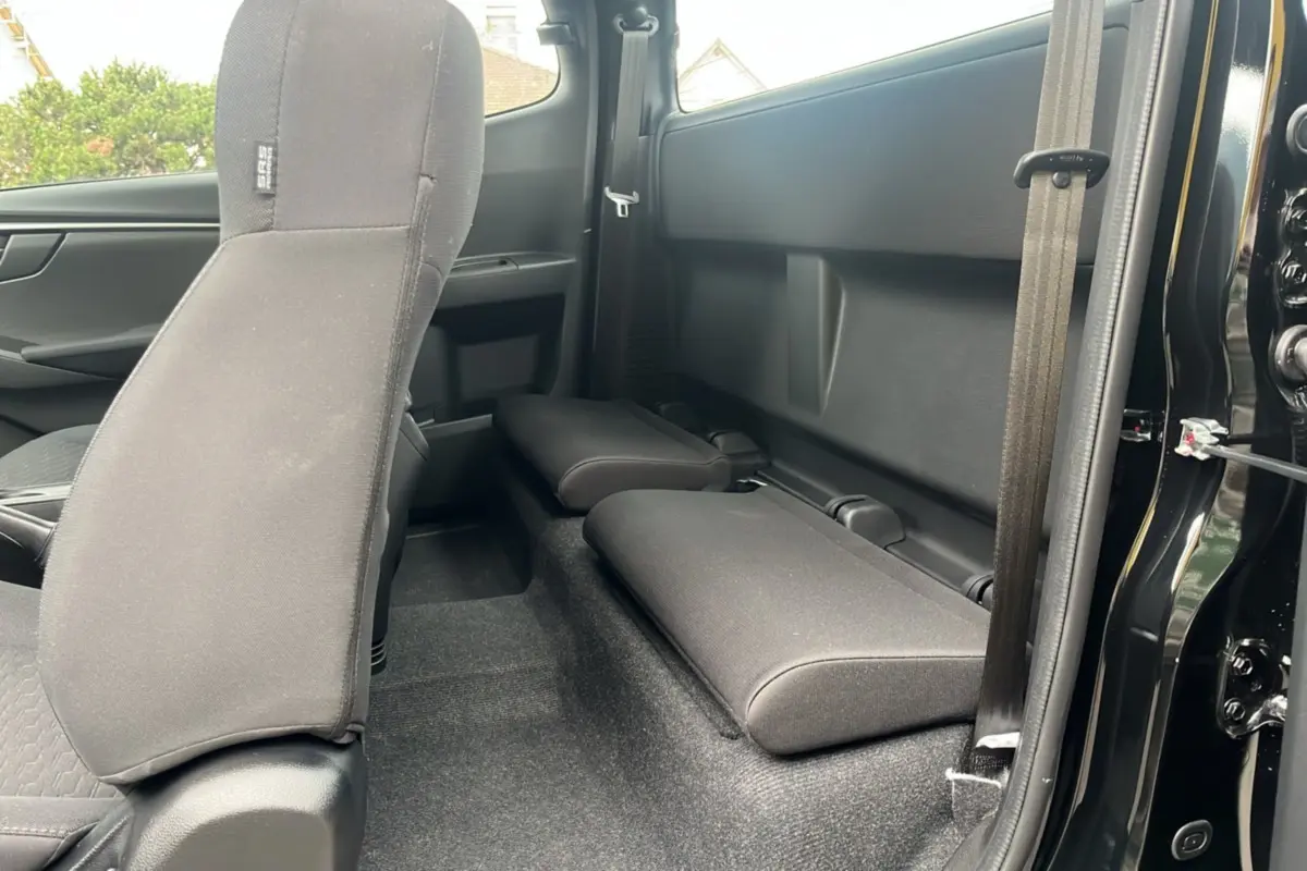 Vue intérieure côté droit du pick-up Isuzu D-MAX 2026 noir, montrant les strapontins arrière rabattus et la sellerie tissu noire.
