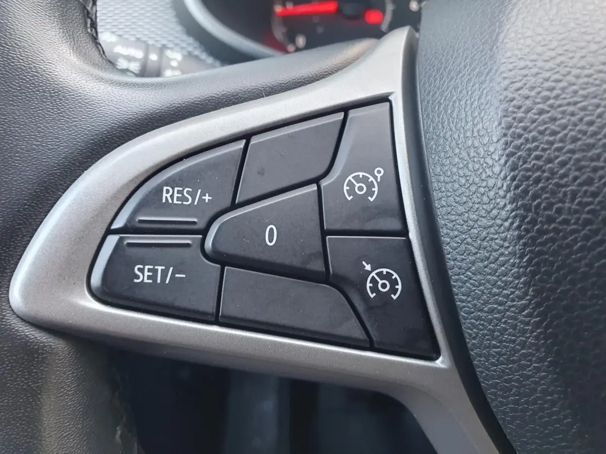 Gros plan sur les commandes du régulateur de vitesse au volant d’une Dacia Sandero gris urbain 2024.
