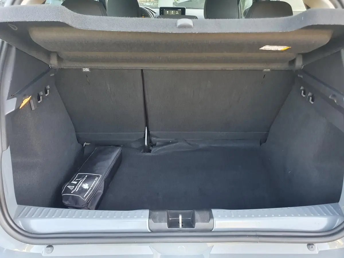 Coffre ouvert vu de l'arrière d'une Dacia Sandero gris urbain 2024, avec un kit de secours noir posé à gauche.