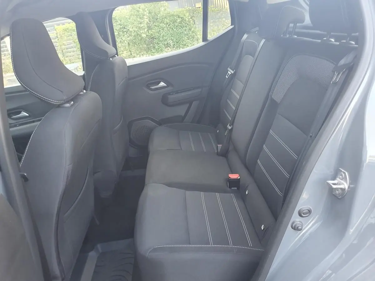 Vue intérieure arrière côté droit de la Dacia Sandero 2024 gris urbain, montrant les sièges arrière en tissu noir avec surpiqûres blanches.