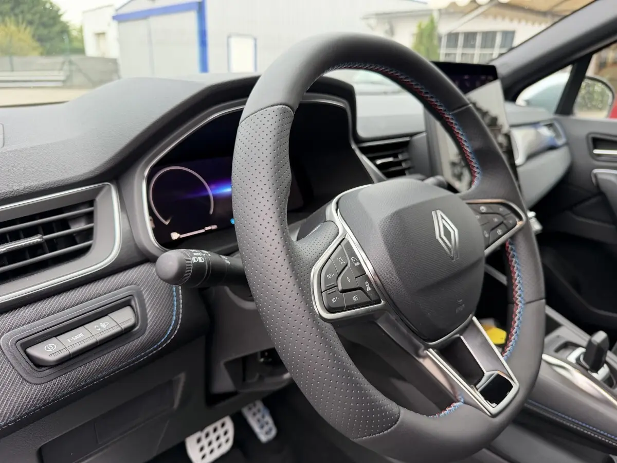 Vue intérieure centrée sur le volant cuir perforé avec surpiqûres bleues et tableau de bord numérique du Renault Captur bleu esprit Alpine.