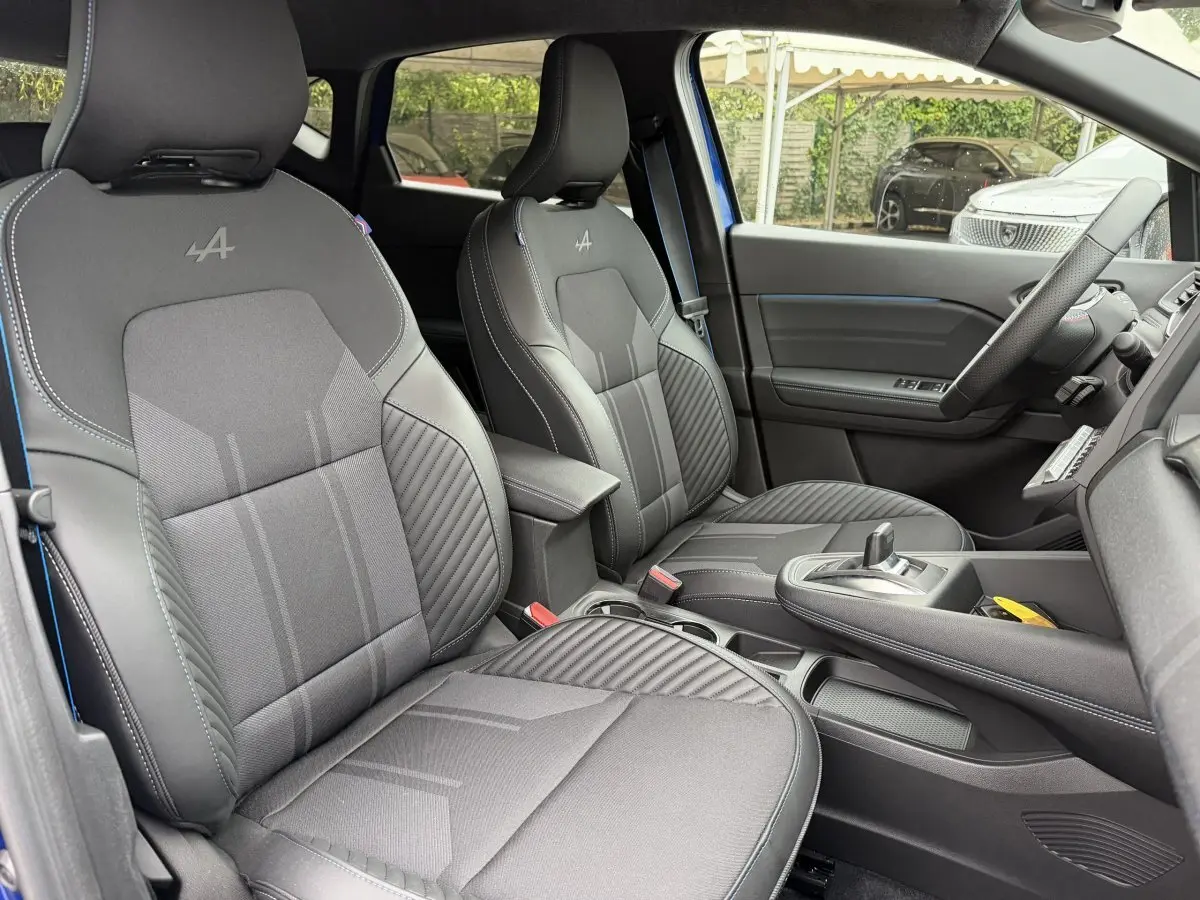 Vue intérieure avant du Renault Captur Esprit Alpine bleu, sièges noirs avec logo Alpine brodé sur appuie-têtes.