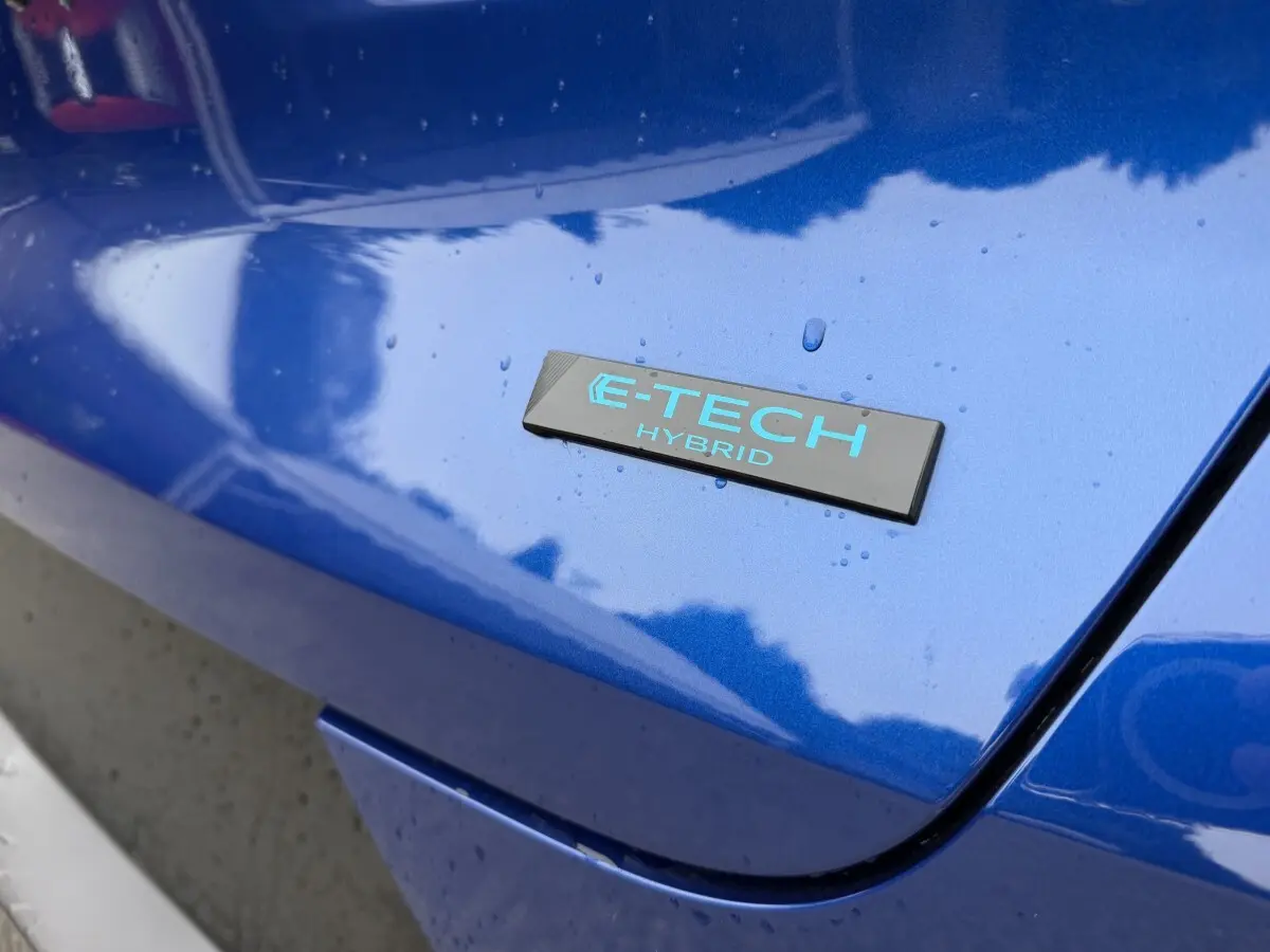 Gros plan sur l'emblème E-TECH Hybrid bleu clair sur la carrosserie bleue brillante d'une Renault Captur.