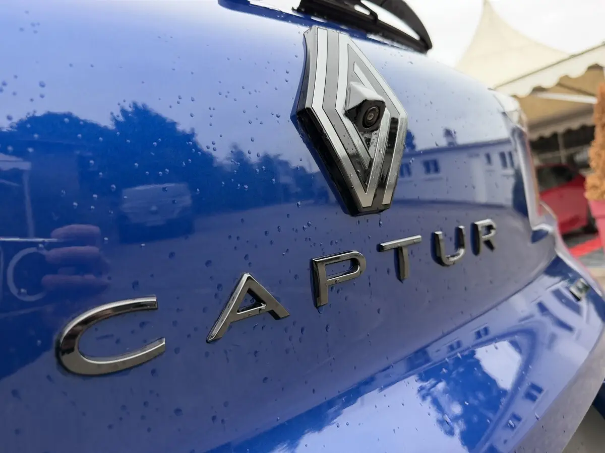 Gros plan sur le logo Renault et le nom Captur en lettres chromées sur la malle arrière bleu brillant avec gouttes d'eau.