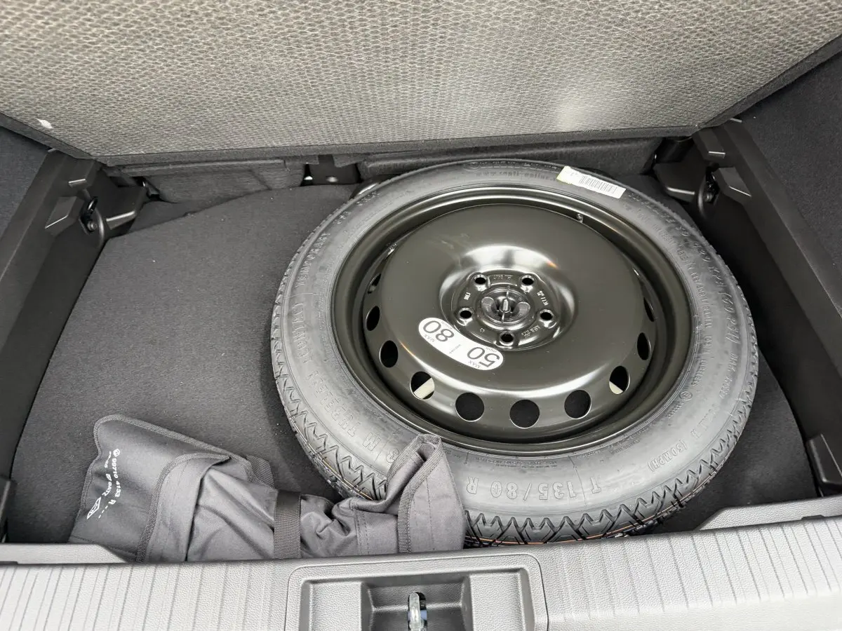 Vue plongeante sur la roue de secours noire et l’espace de rangement dans le coffre du Renault Captur bleu esprit Alpine.