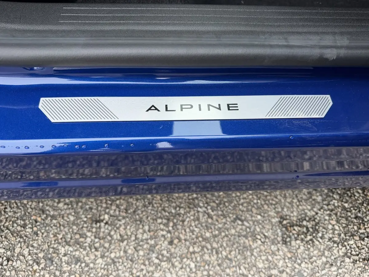 Gros plan sur la plaque Alpine sur le seuil de porte bleu d'un Renault Captur esprit Alpine full hybrid.