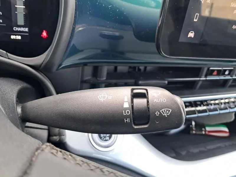 Le levier d'essuie-glace de la FIAT 500C électrique 2021 en gros plan, tableau de bord vert foncé métallique visible en arrière-plan.