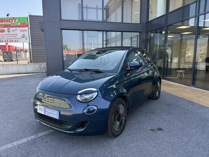 Fiat 500C 118 cv icone électrique vert foncé métal vue 3/4 avant droit devant un bâtiment vitré