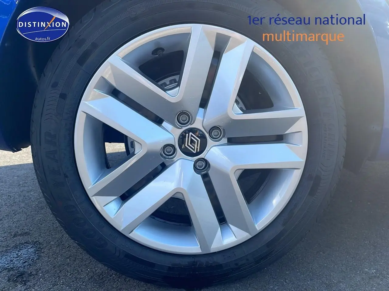Gros plan sur la jante alliage argentée d'une Renault Clio V bleu iron, mettant en valeur le logo au centre.