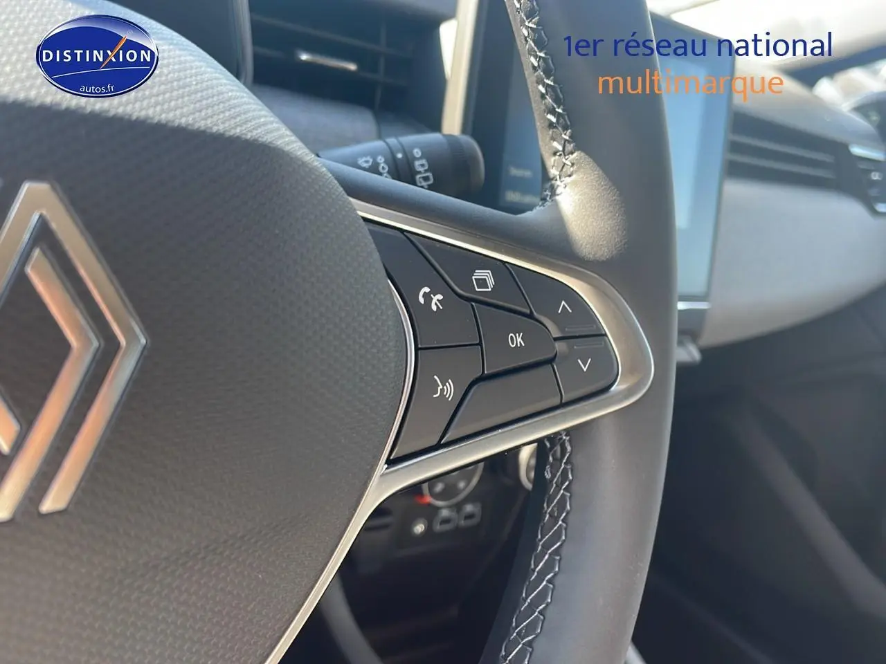 Gros plan sur les commandes du volant multifonction de la Renault Clio V bleu iron, avec écran tactile en arrière-plan.