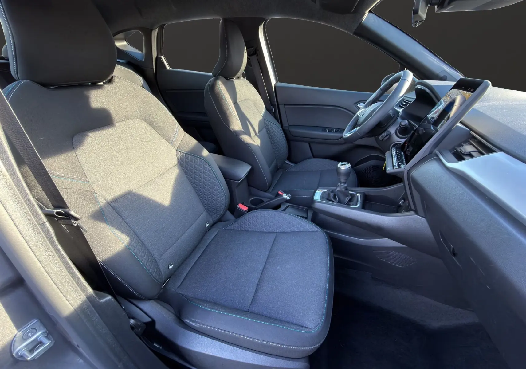 Vue intérieure côté gauche du Renault Captur 2024 gris Cassiopée, montrant sièges tissu et boîte manuelle.