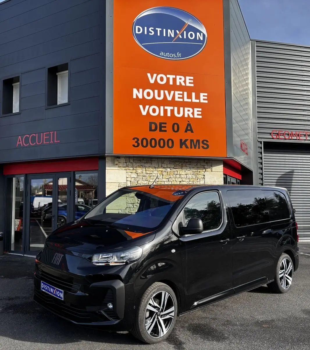Fiat Scudo Fourgon noir en 3/4 avant droit, stationné devant un bâtiment avec enseigne orange Distinxion.
