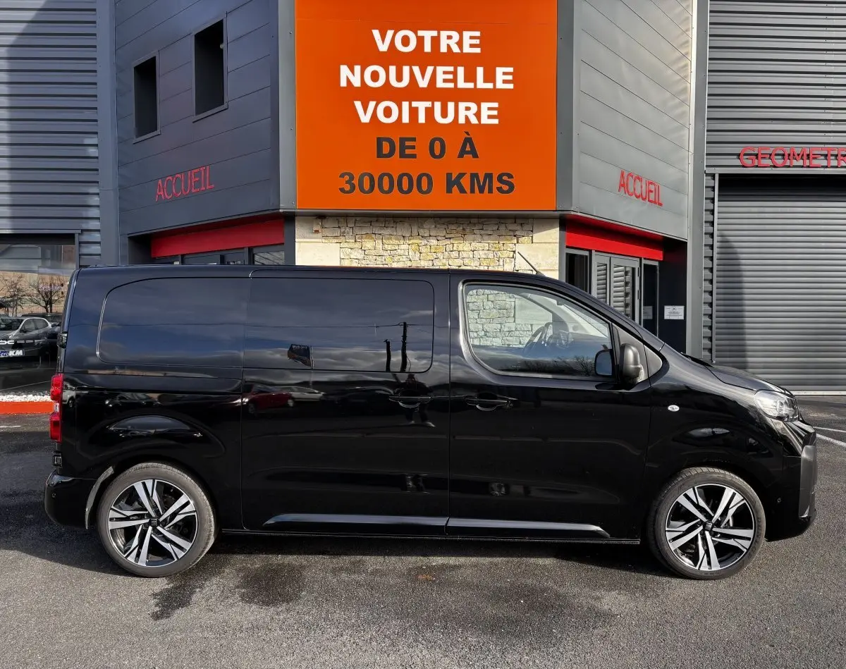 Profil droit d’un FIAT Scudo Fourgon noir 2025, avec jantes alliage et vitres teintées, stationné devant un bâtiment commercial.