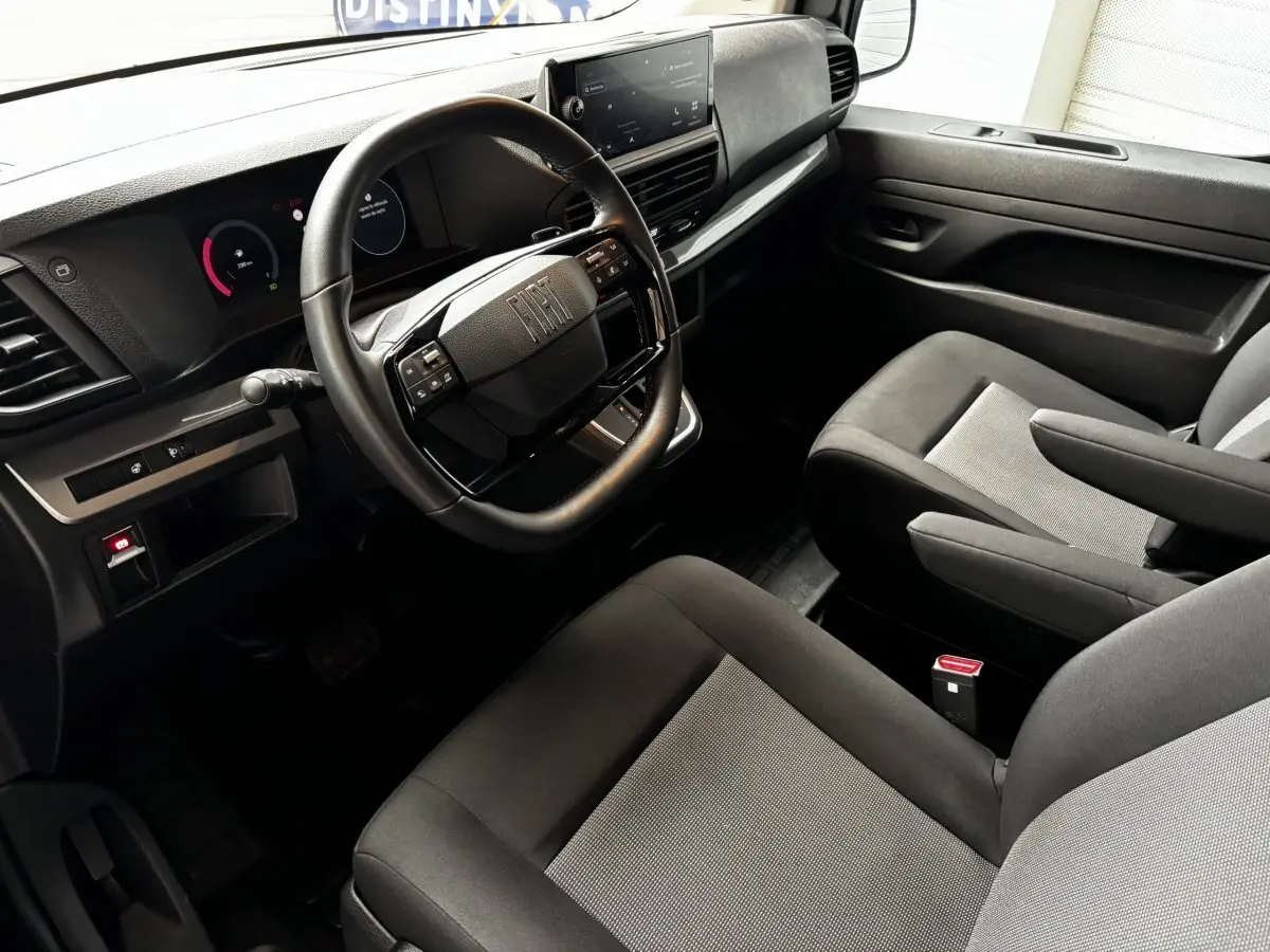 Vue intérieure côté conducteur du Fiat Scudo Fourgon 2025, tableau de bord moderne avec volant multifonction noir et sièges gris.