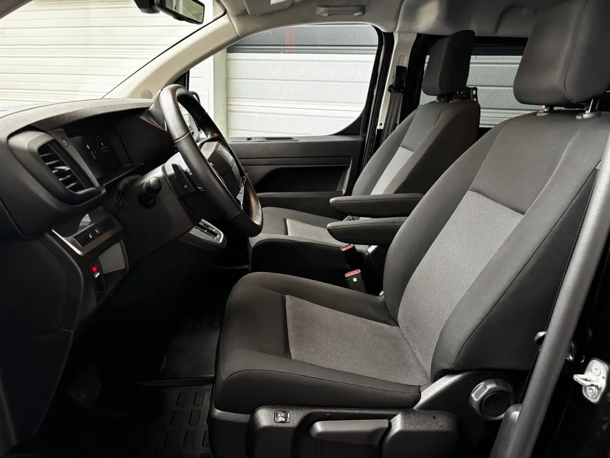 Vue intérieure côté conducteur du Fiat Scudo Fourgon 2025 noir, sièges tissu gris avec accoudoirs et tableau de bord moderne.