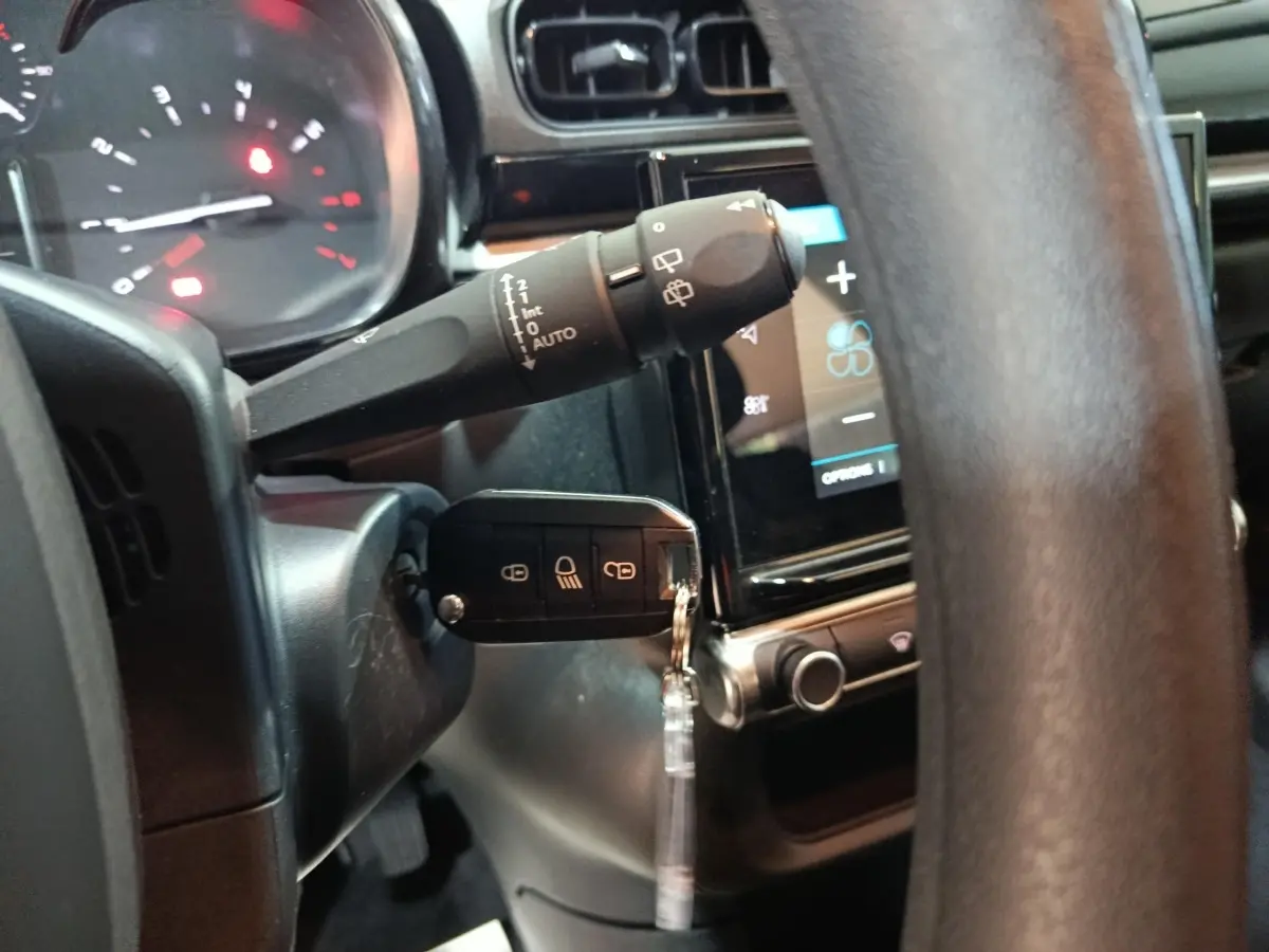 Vue intérieure centrée sur le volant réglable et la clé insérée d'une Citroën C3 gris foncé, tableau de bord tactile visible.