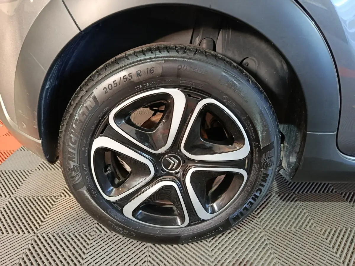 Gros plan sur la roue avant droite d'une Citroën C3 gris foncé avec jante alliage noire et argentée.