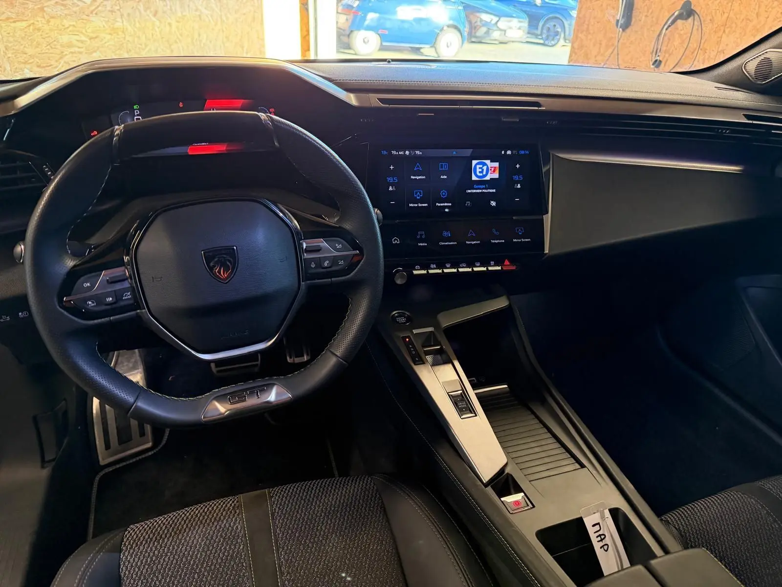 Vue intérieure de la Peugeot 408 GT 2025, tableau de bord noir avec volant compact et écran tactile central lumineux.