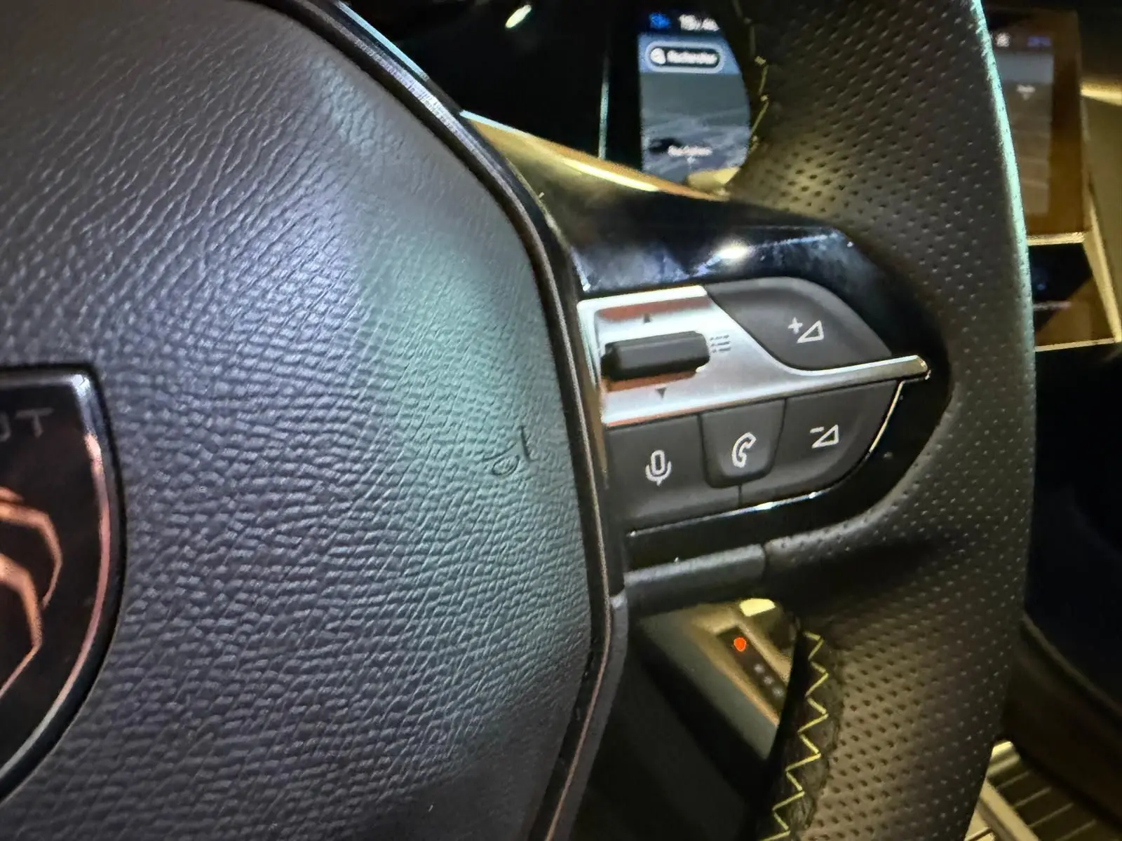 Gros plan sur le volant noir perforé avec commandes intégrées et écran tactile flou en arrière-plan.