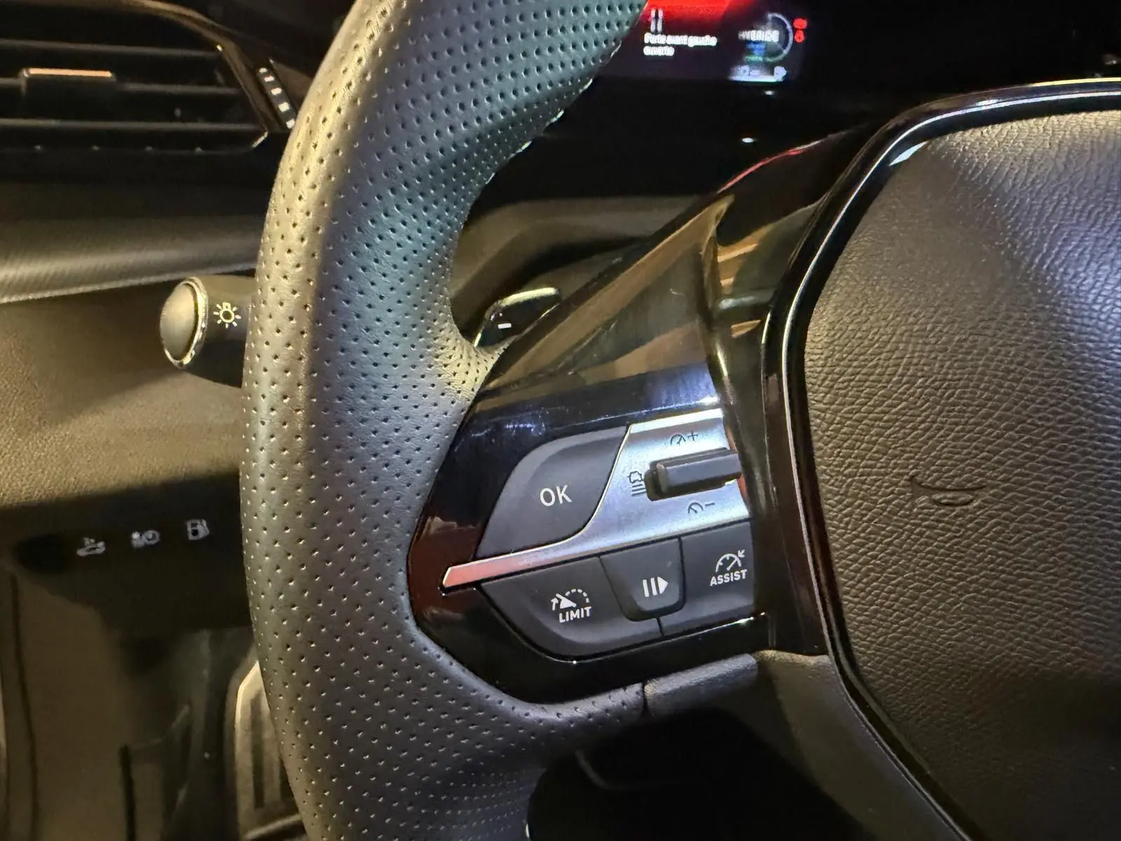 Gros plan sur le volant perforé noir avec commandes multifonctions et tableau de bord numérique partiel de la Peugeot 408 gris Selenium.