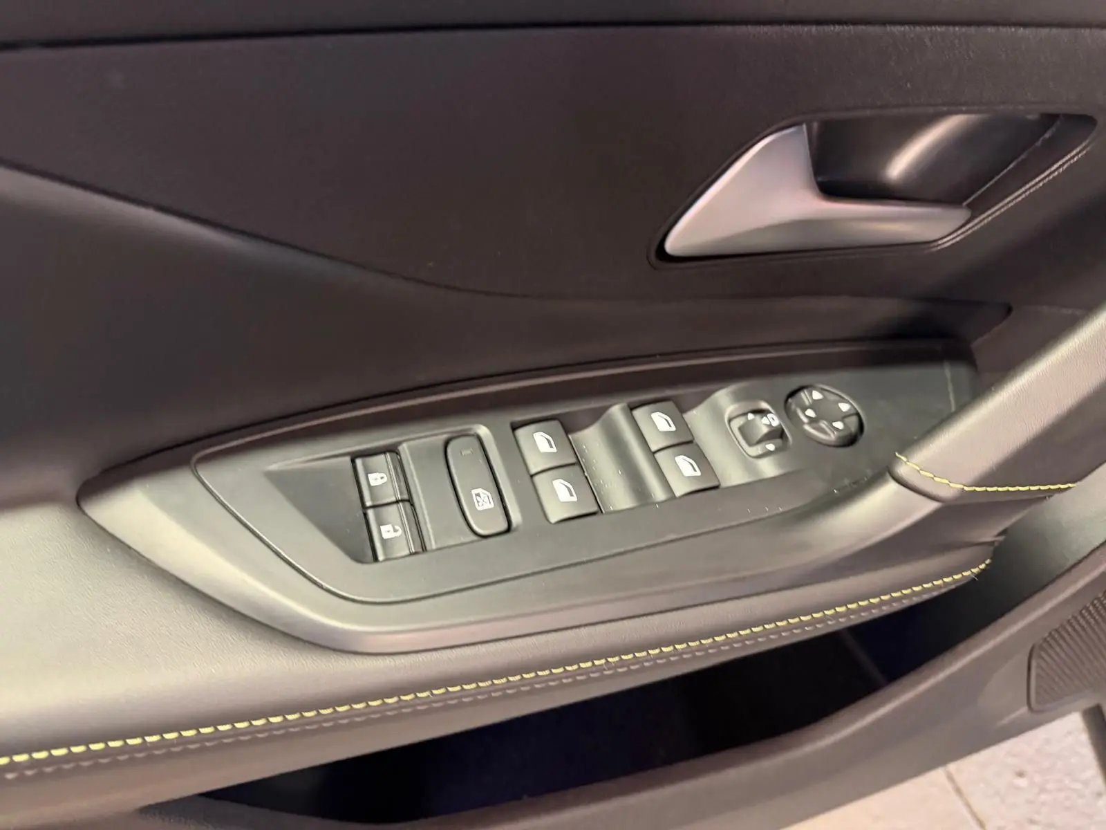 Détail des commandes de lève-vitres et rétroviseurs sur la porte avant gauche du Peugeot 408 gris, avec surpiqûres vertes.