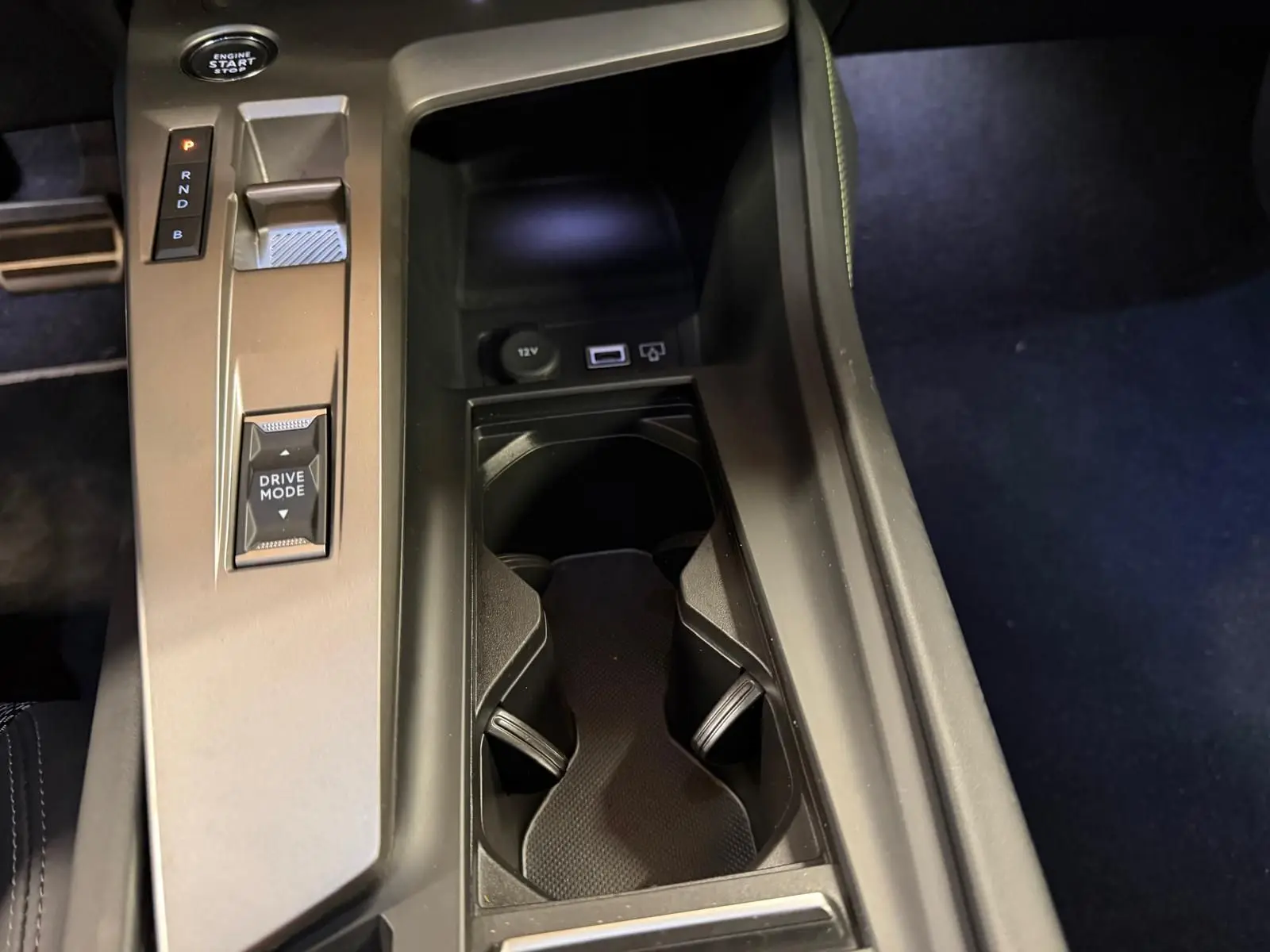 Vue rapprochée de la console centrale noire avec sélecteur de modes et porte-gobelets du Peugeot 408 gris 2025 hybride rechargeable.