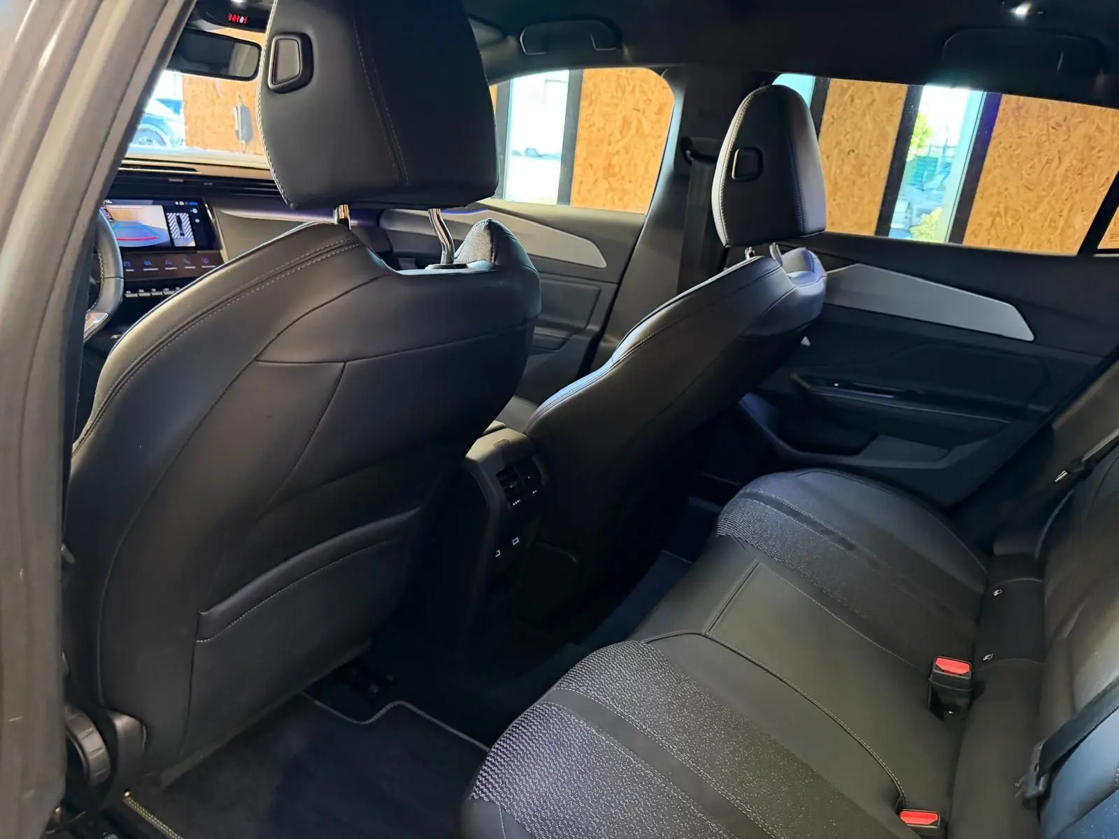 Vue intérieure arrière droite de la Peugeot 408 2025, sièges noirs tri-matières avec surpiqûres vertes et détails aluminium.