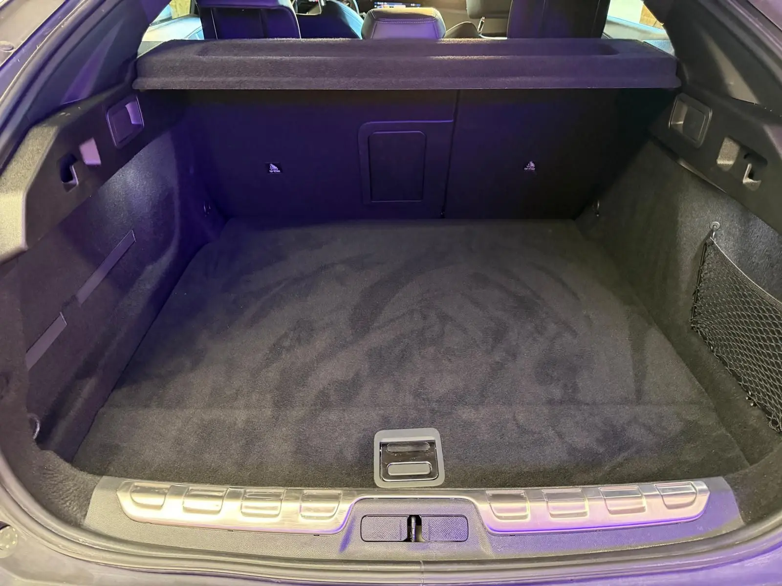 Coffre ouvert vu de l'arrière d'une Peugeot 408 gris, avec tapis de sol noir et filet de rangement latéral.