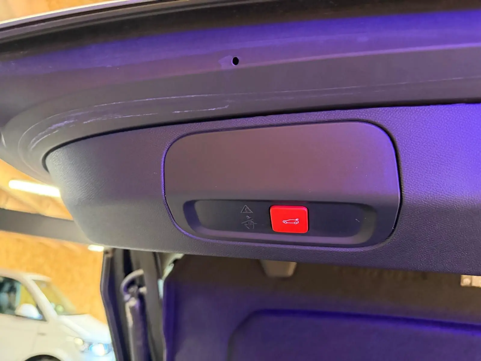 Gros plan sur le bouton rouge d'ouverture motorisée du hayon d'une Peugeot 408 gris Selenium, intérieur coffre visible.