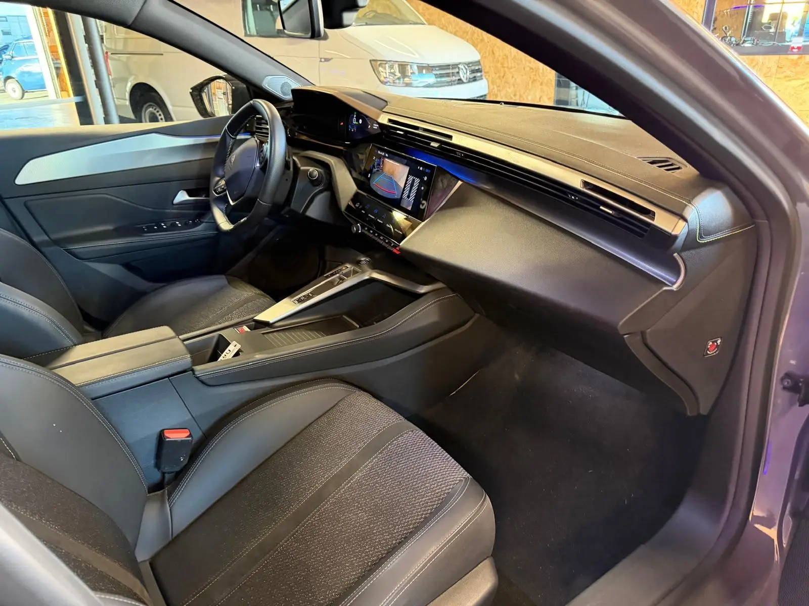 Vue intérieure côté conducteur de la Peugeot 408 2025 gris, avec tableau de bord moderne et écran tactile central allumé.