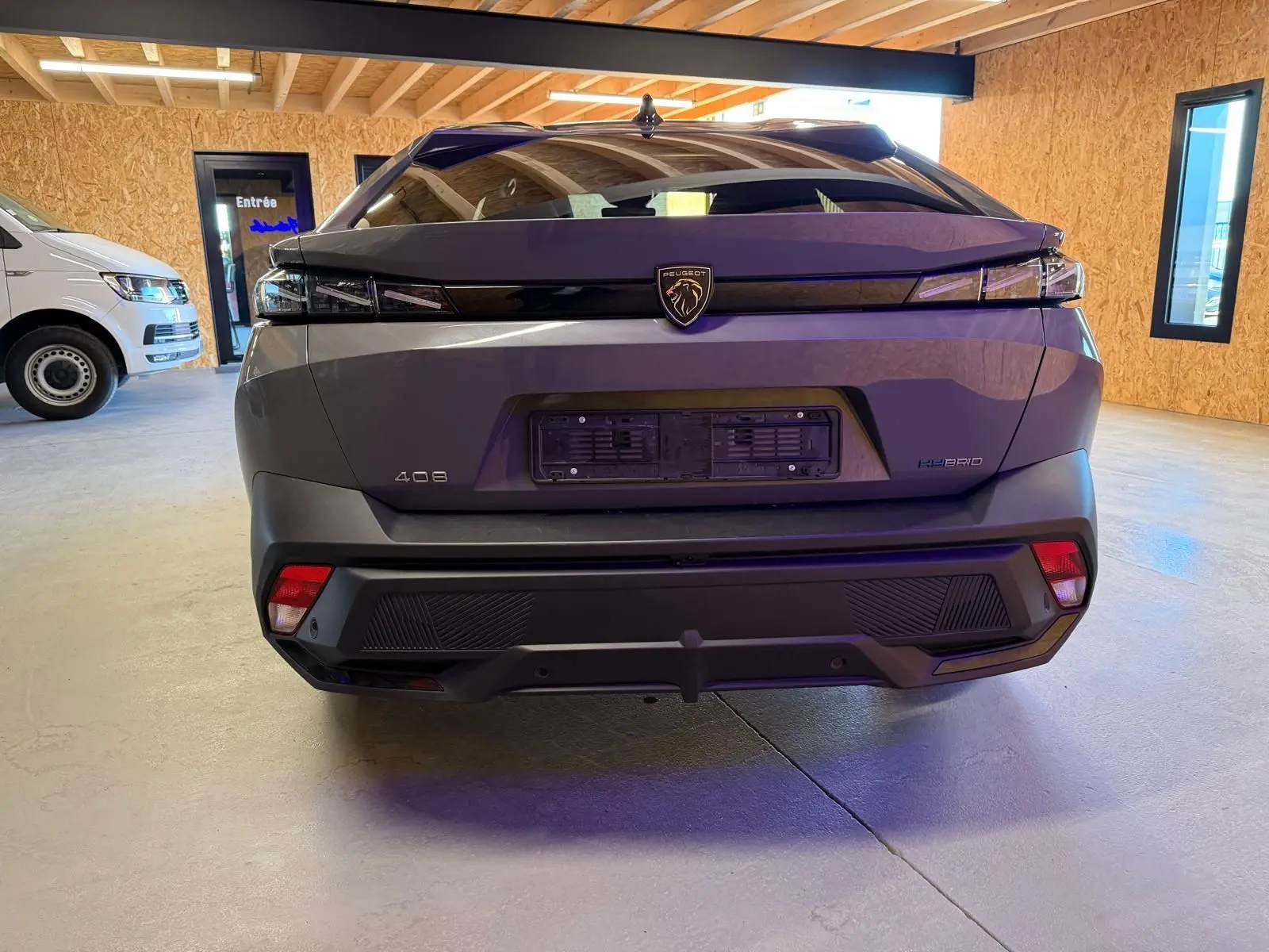 Vue arrière d'une Peugeot 408 gris Selenium avec feux arrière à effet griffe et badge Hybrid visible en intérieur.