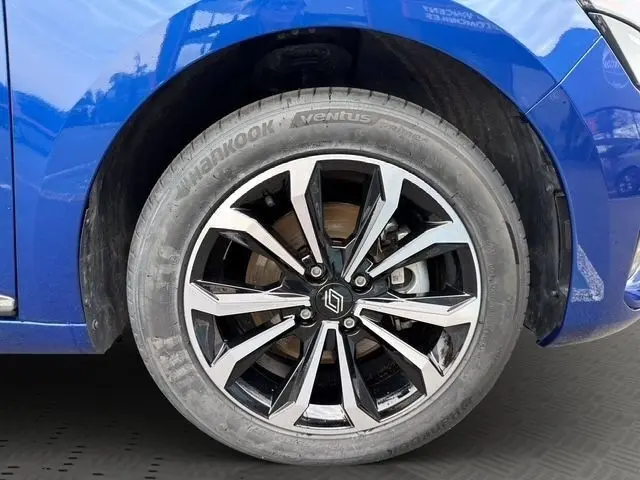 Gros plan sur la roue avant droite d'une Renault Clio Techno E-Tech bleu, avec jante alliage noire et argentée au design moderne.