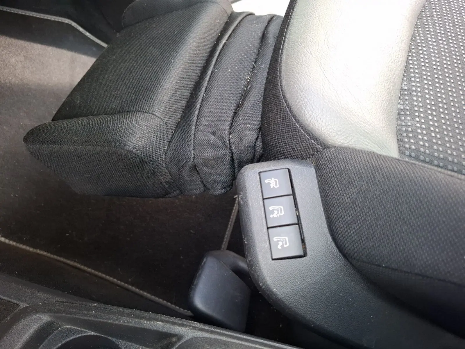 Boutons de réglage des sièges massants sur le côté droit d’un siège avant en cuir et tissu noir du Citroën C4 Picasso gris clair.