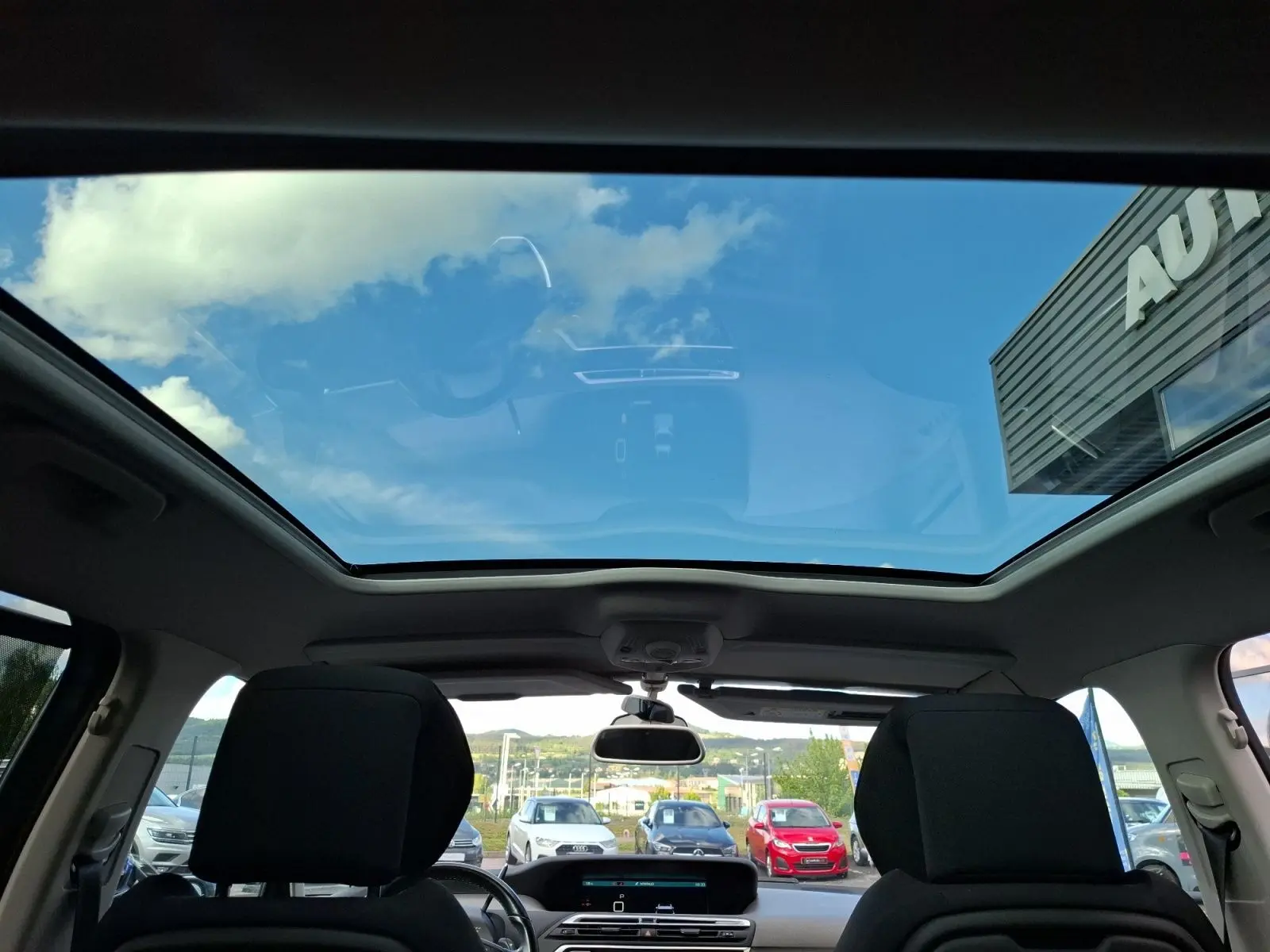 Vue intérieure du toit panoramique du Citroën C4 Picasso gris clair, avec sièges avant et tableau de bord visibles.