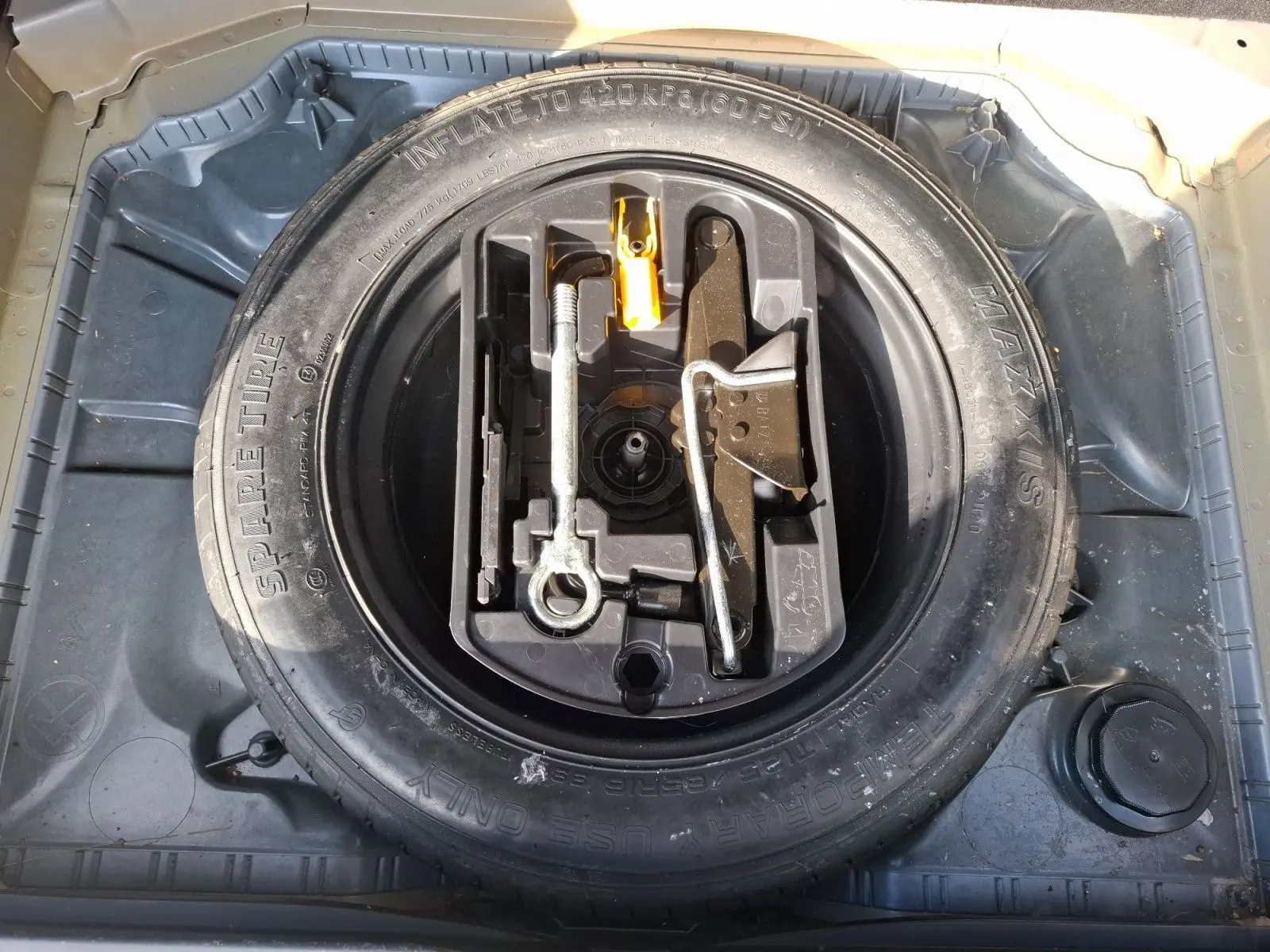 Vue plongeante sur la roue de secours et le kit d'outils dans le coffre d'une Citroën C4 Picasso gris clair 2018.