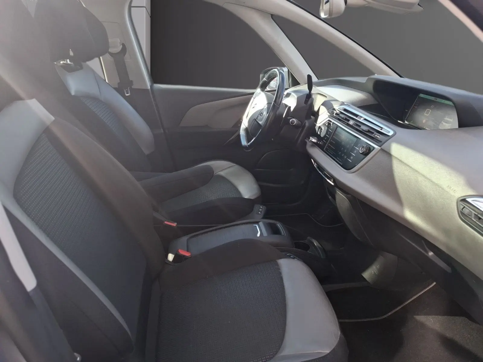 Vue intérieure côté conducteur de la Citroën C4 Picasso gris clair, avec sellerie cuir et tissu et tableau de bord moderne.