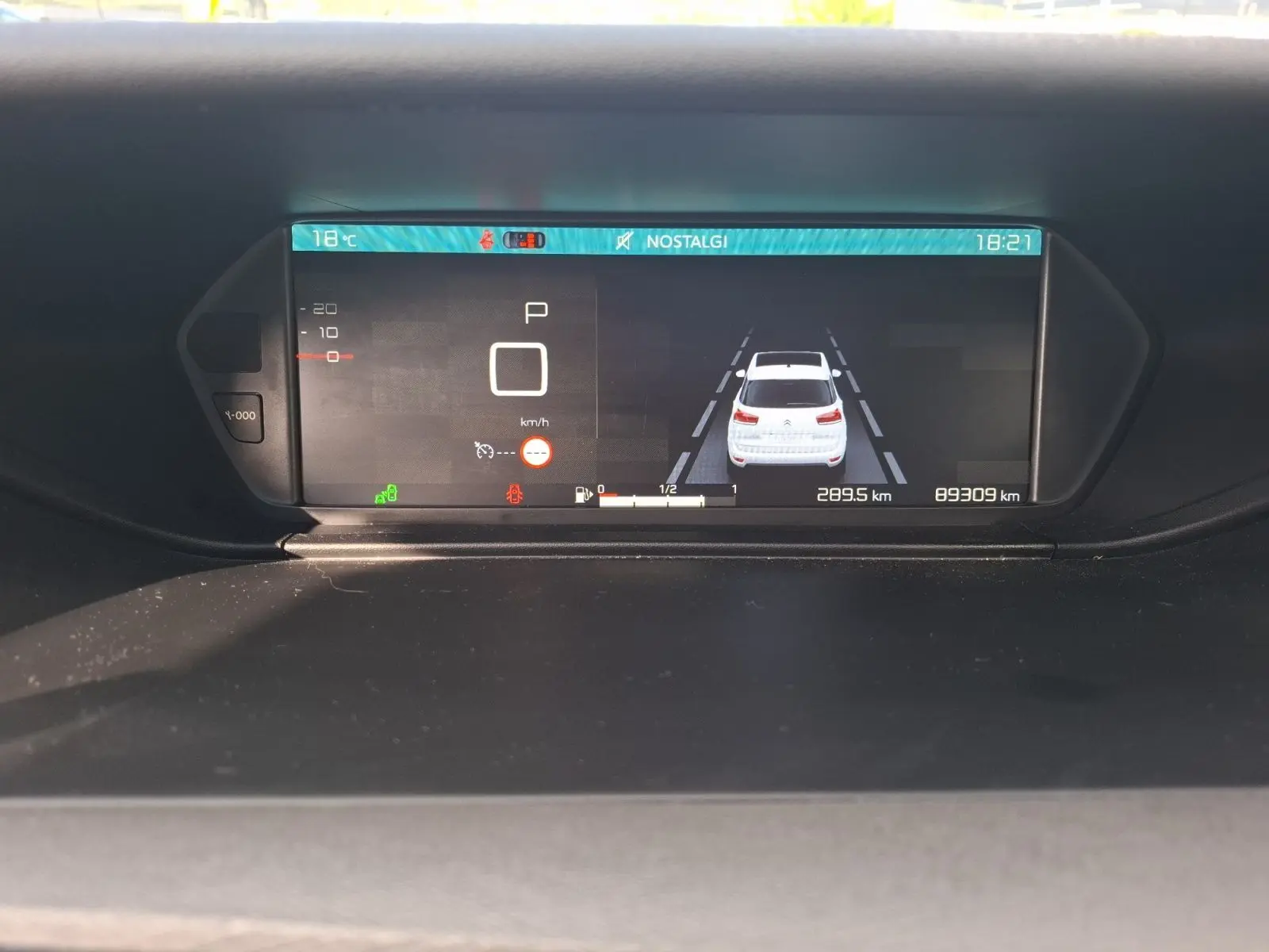 Affichage numérique du tableau de bord de la Citroën C4 Picasso montrant la voiture blanche en vue arrière et les informations de conduite.