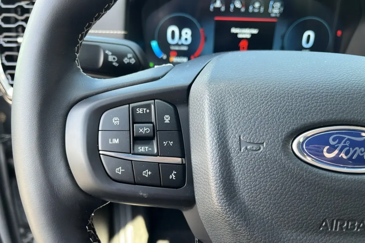Gros plan sur le volant multifonctions en cuir du Ford Ranger gris, avec commandes de régulateur et logo Ford visible.