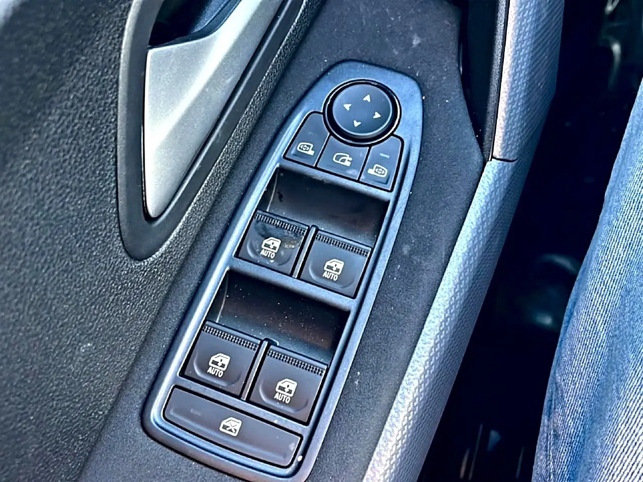 Gros plan sur les commandes des vitres électriques et rétroviseurs sur la porte côté gauche d’un Dacia Duster noir.