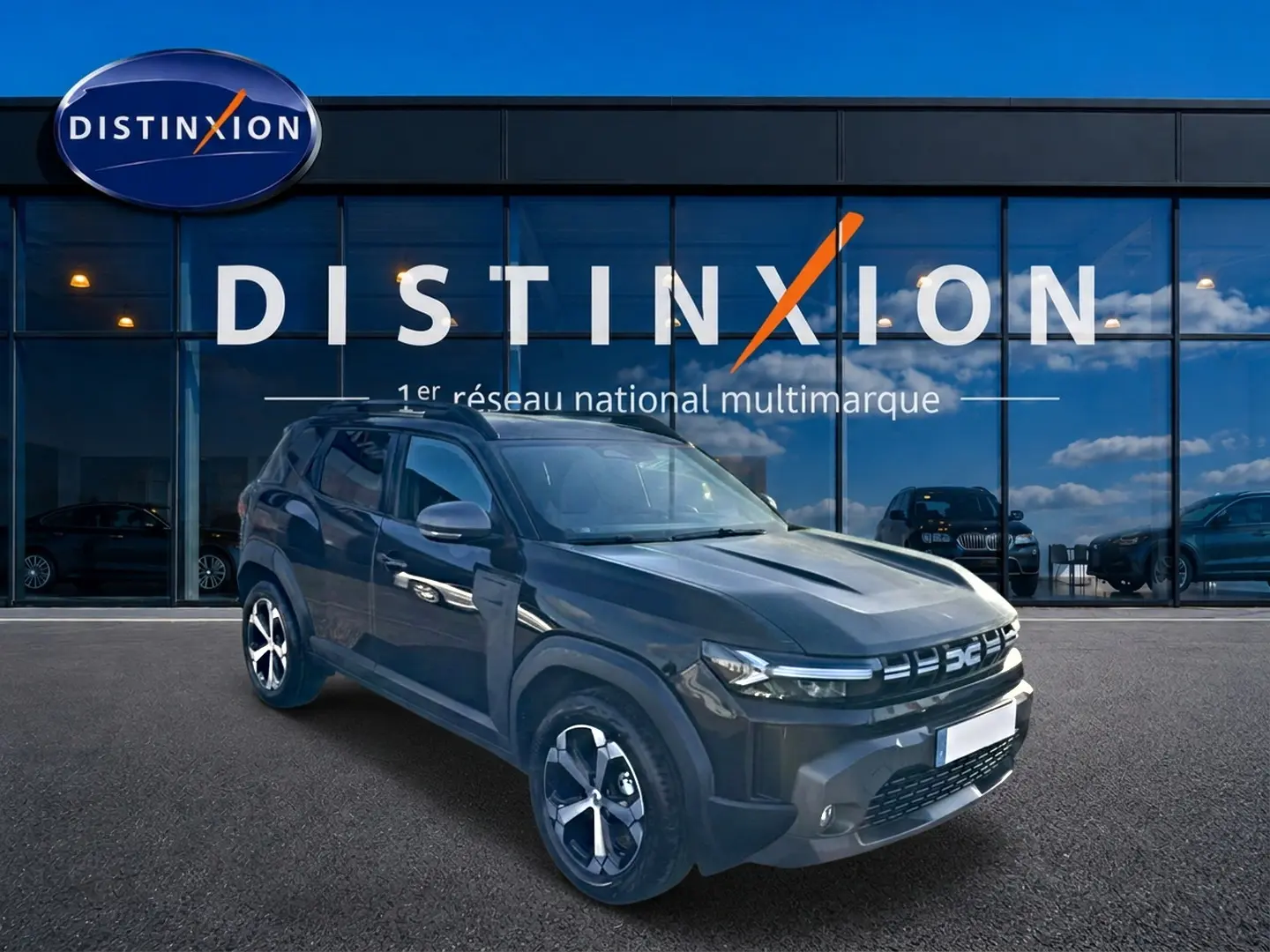 Dacia Duster noir en 3/4 avant droit, avec jantes alu et barres de toit, devant une vitrine Distinxion.