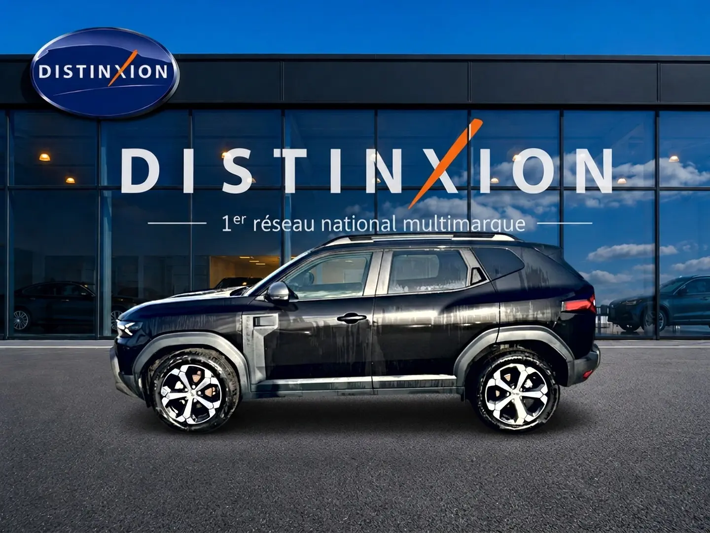Profil côté gauche du Dacia Duster noir 2026 avec jantes alu, garé devant une vitrine Distinxion.