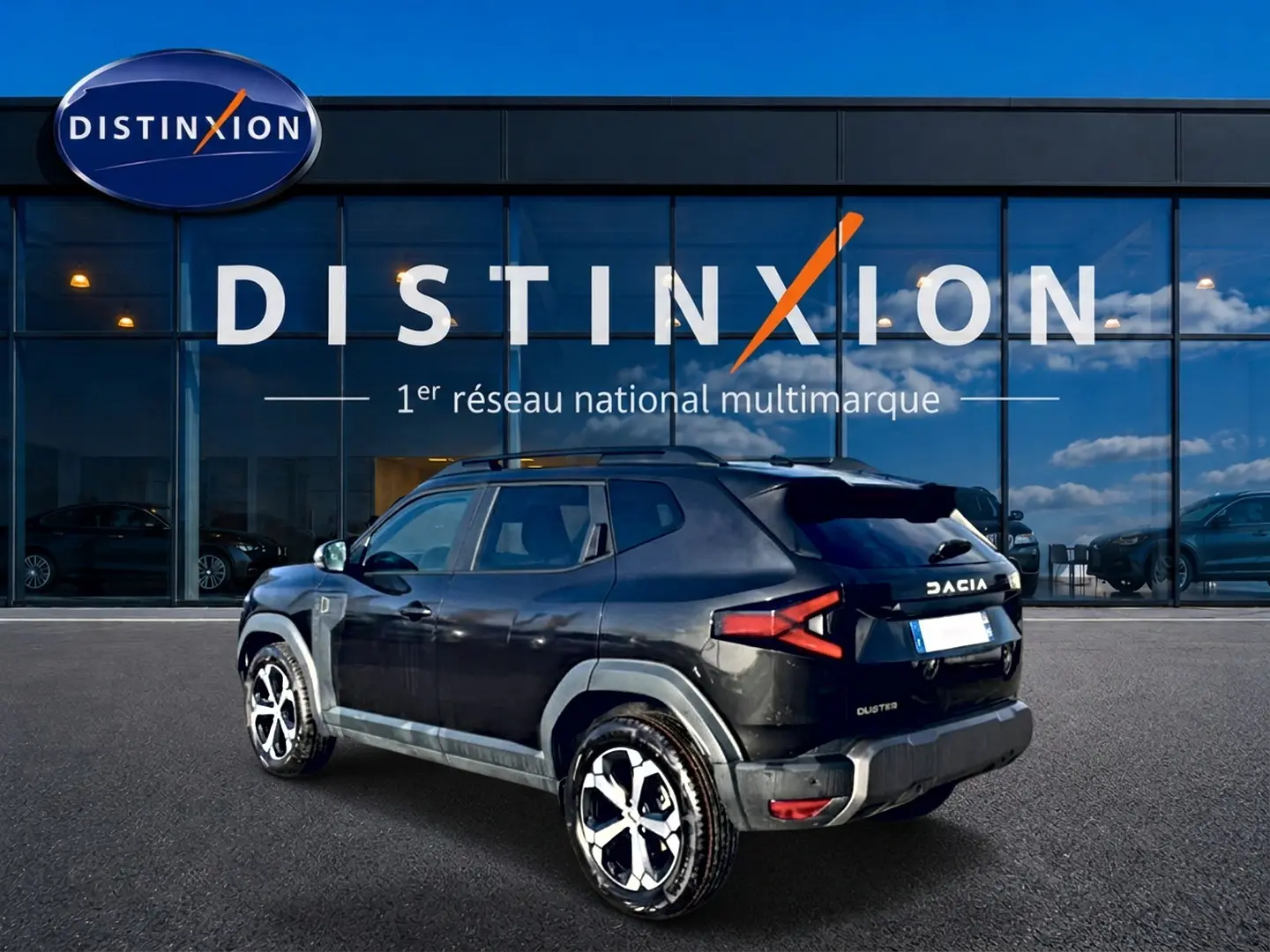Vue 3/4 arrière droite du Dacia Duster noir 2026 avec jantes alu et barres de toit devant un showroom Distinxion.