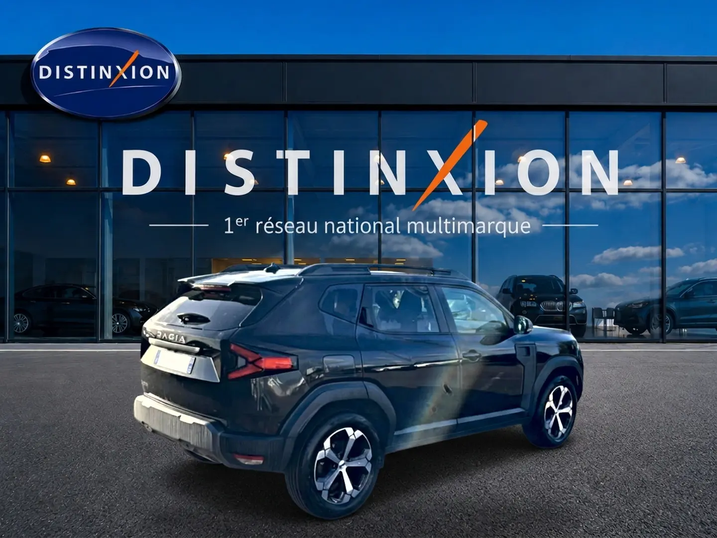Vue 3/4 arrière droite d'un Dacia Duster noir 2026 avec jantes alu, barres de toit et becquet arrière visible.
